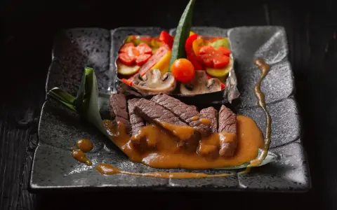 Straccetti di manzo succulenti su un piatto scuro, accompagnati da verdure miste e una salsa cremosa.