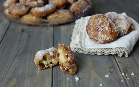 Frittelle di riso ricetta della nonna: dolcetti dorati e zuccherati, uno aperto rivela l'interno soffice e i chicchi d'uva passa.