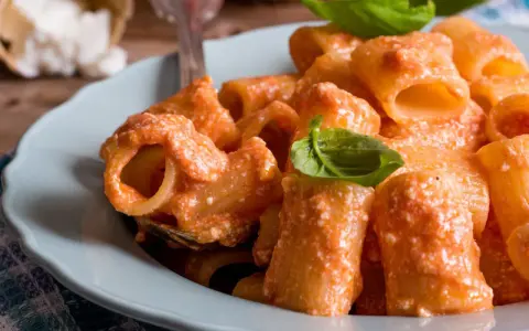 Piatto di pasta ricotta e pomodorini, condita con una cremosa salsa e guarnita con foglie di basilico fresco.