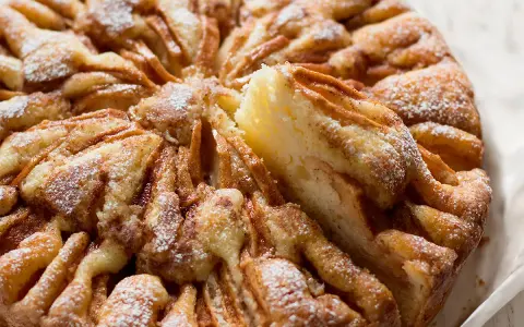 Una deliziosa torta di mele, cosparsa di zucchero a velo, con una fetta sollevata che rivela la morbida consistenza.