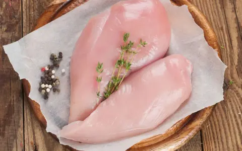 Due petti di pollo crudi, freschi e succulenti, adagiati su carta forno con pepe misto e rametti di timo.