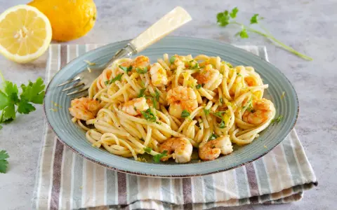Un piatto di pasta con gamberetti, condita con limone e prezzemolo, accompagnata da limoni freschi e parmigiano.