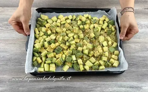 Zucchine gratinate al forno pronte per essere infornate, tagliate a cubetti e cosparse di pangrattato.