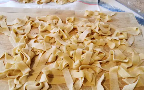 Fettuccine fresche, tagliatelle fatte in casa sparse su un tagliere di legno, pronte per essere cucinate.