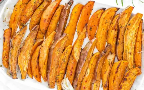 Patate dolci al forno, tagliate a spicchi e condite con erbe aromatiche, servite su un piatto bianco.