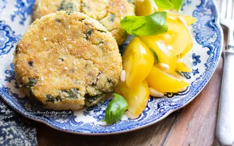 Hamburger di zucchine dorati e croccanti, serviti con pomodorini gialli e basilico fresco su un piatto blu e bianco.