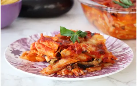 Piatto di pasta alla siciliana con melanzane, pomodoro e basilico, appena sfornata.