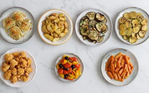 Sette piatti di verdure in friggitrice ad aria: finocchi gratinati, patate arrosto, melanzane, zucchine, cavolfiore fritto, peperoni e carote.