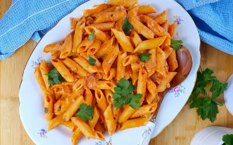 Piatto di penne al baffo cremose, guarnite con prezzemolo fresco, pronte per essere gustate.