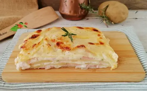 Una fetta di parmigiana di patate dorata e filante, con strati di patate, prosciutto e besciamella, guarnita con rosmarino.