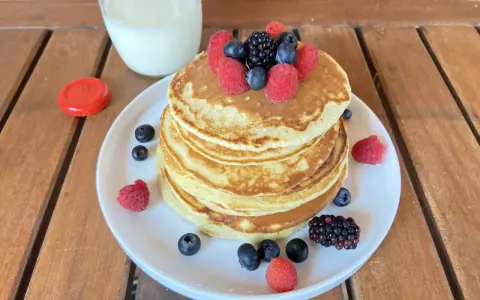 Pila di pancake senza zucchero guarnita con frutti di bosco freschi, accompagnata da un bicchiere di latte.