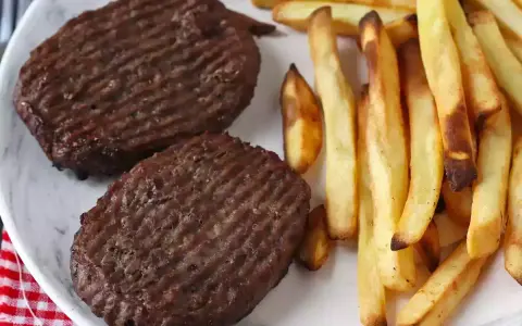 Due hamburger in friggitrice ad aria con patatine fritte dorate su un piatto bianco.
