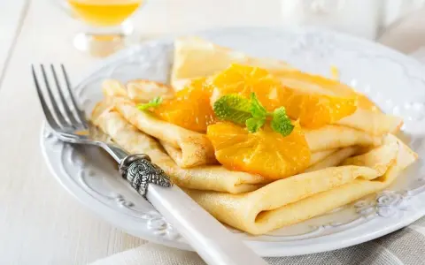 Deliziose crepes senza uova, guarnite con spicchi d'arancia succosa e foglioline di menta fresca. Un piatto leggero e gustoso.