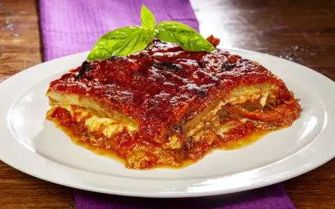 Una fetta di parmigiana di melanzane napoletana, ricca e saporita, guarnita con basilico fresco.