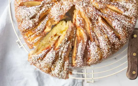 Deliziosa torta di mele in friggitrice ad aria, spolverata di zucchero a velo, con una fetta tagliata per mostrare il morbido interno.