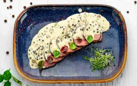 Fette fettine di filetto al pepe verde, ricoperte da una cremosa salsa, guarnite con germogli freschi e foglie verdi.