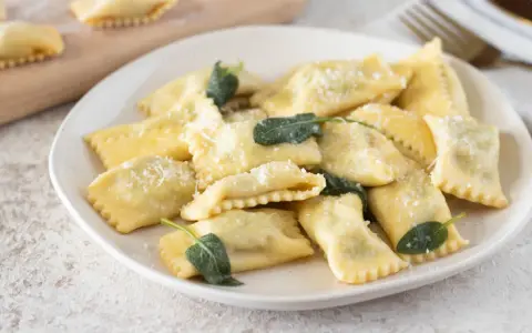 Piatto di ravioli del plin, dorati e spolverati di parmigiano, guarniti con foglie di salvia fresca.