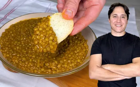 Un uomo sorride mentre un pezzo di pane intinge in una ciotola di saporite lenticchie in umido.