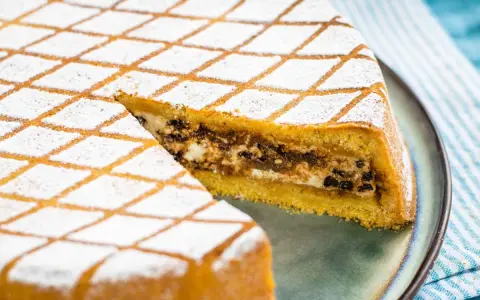 Una fetta di cassata al forno, con la sua copertura a rombi di zucchero a velo, rivela un ripieno goloso di ricotta e cioccolato.