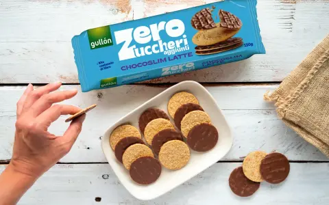 Biscotti senza zucchero Gullón Chocoslim Latte, alcuni ricoperti di cioccolato, su un piatto bianco. Una mano ne prende uno.