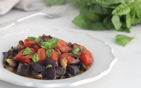 Un piatto invitante di melanzane a funghetto con pomodorini e basilico fresco, pronto per essere gustato.