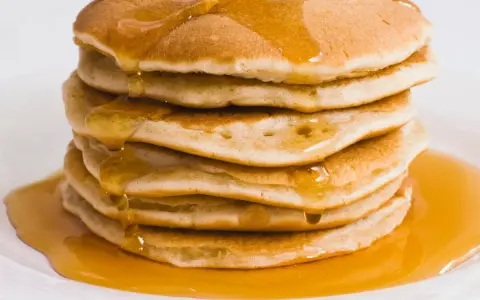 Pila di pancake dorati, inzuppati di sciroppo d'acero. Perfetti per una ricetta pancake proteici sana e golosa.