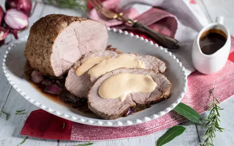 Arrosto di vitello morbido con sughetto benedetta, servito su un piatto bianco con cipolle rosse e rosmarino.
