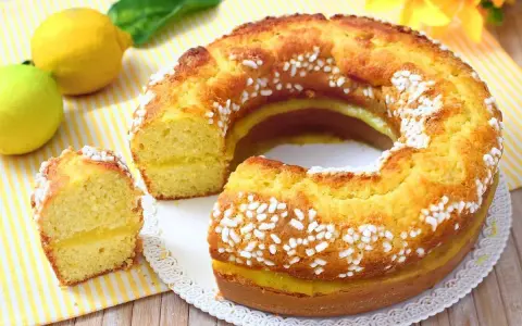 Un soffice ciambellone al limone, decorato con perline di zucchero, con una fetta tagliata che rivela un ripieno cremoso.