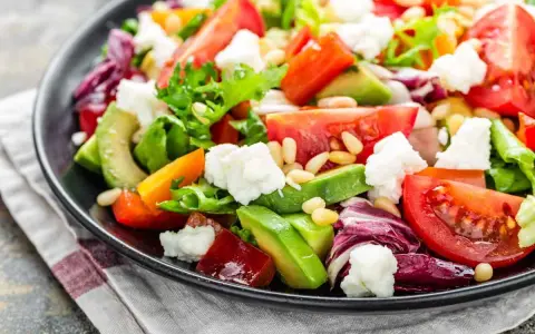 Insalata fresca con pomodori, lattuga, formaggio e avocado a fette, guarnita con pinoli.