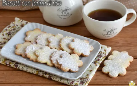 Biscotti con farina di riso a forma di fiore, spolverati di zucchero a velo, accanto a una tazza di tè e una teiera.