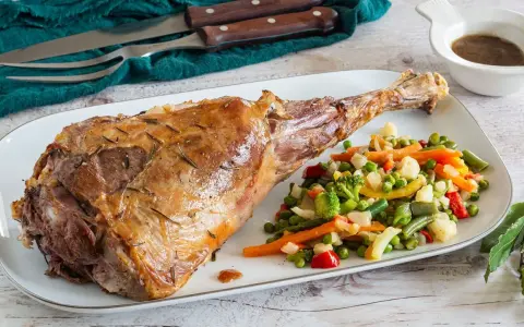 Succulento agnello al forno, dorato e profumato, servito con un contorno di verdure miste colorate.