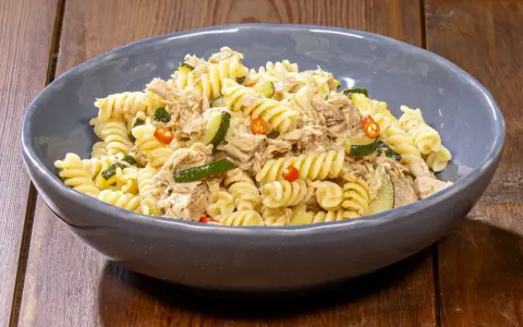 Fusilli con zucchine, tonno e peperoncino in una ciotola blu su un tavolo di legno. Un piatto semplice e gustoso.