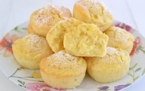 Morbidi muffin alle mele, spolverati di zucchero a velo, su un piatto fiorito. Uno è tagliato a metà, mostrando la soffice mollica.