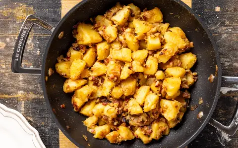 Patate in tecia dorate e croccanti, con pezzetti di pancetta e cipolla, pronte per essere gustate.