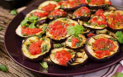 Fette di melanzane grigliate condite con salsa di pomodoro e basilico, un piatto invitante di melanzane alla pizzaiola.
