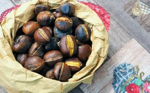 Castagne in friggitrice ad aria, pronte per essere gustate. Un sacchetto di carta marrone trabocca di castagne calde e dorate, alcune con tagli che rivelano il loro interno morbido.