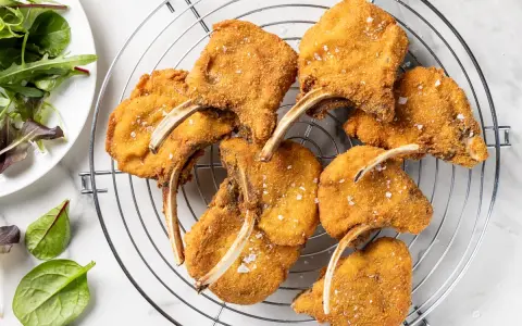 Deliziose costolette d'agnello fritte, dorate e croccanti, cosparse di sale grosso, su una griglia. Accanto, un'insalata fresca.