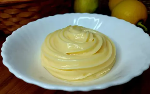 Una spirale di soffice crema al limone in una ciotola bianca, con limoni e uova sullo sfondo.