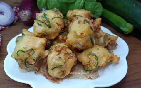 Frittelle di zucchine dorate e croccanti, pronte per essere gustate. Sullo sfondo, cipolle rosse, basilico fresco e zucchine.