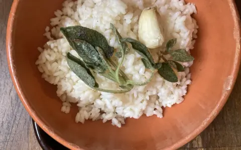 Riso in cagnone, profumato con aglio e salvia croccante, servito in una ciotola di terracotta.