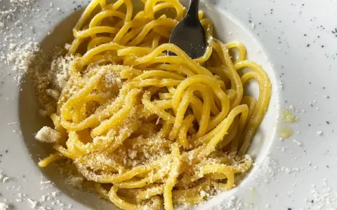 Un piatto di pasta in bianco, spaghetti conditi con formaggio grattugiato e un filo d'olio, pronti per essere gustati.
