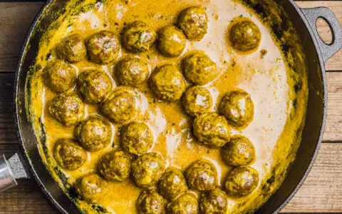 Polpette in bianco cremose in padella, dorate e succulente, immerse in una salsa gialla e invitante.