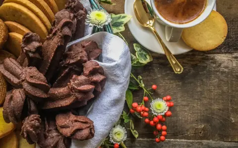 Cesto pieno di biscotti fatti in casa al cioccolato e alla vaniglia, accanto a una tazzina di caffè e bacche rosse.