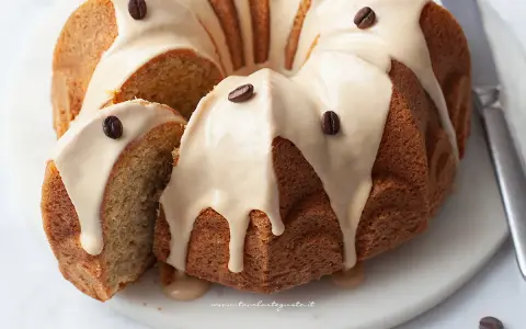 Deliziosa torta al caffè con glassa chiara e chicchi di caffè come decorazione. Una fetta è stata tagliata, mostrando la morbidezza dell'interno.
