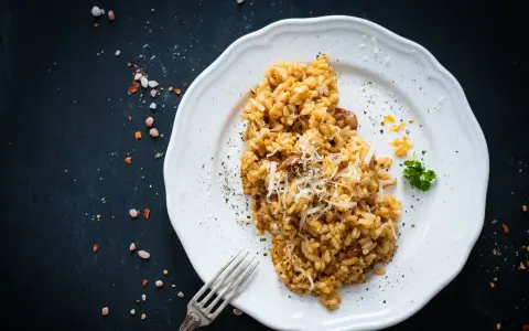 Un piatto di risotto funghi e salsiccia, guarnito con parmigiano grattugiato e prezzemolo, pronto per essere gustato.