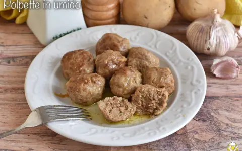 Piatto di polpette in bianco, morbide e succulente, pronte per essere gustate. Sullo sfondo patate e aglio.