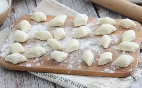 Gnocchi di ricotta freschi, pronti per essere cotti, spolverati di farina su un tagliere di legno.