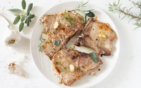 Tre succulente braciole di maiale cotte alla perfezione, guarnite con aglio, rosmarino e salvia.