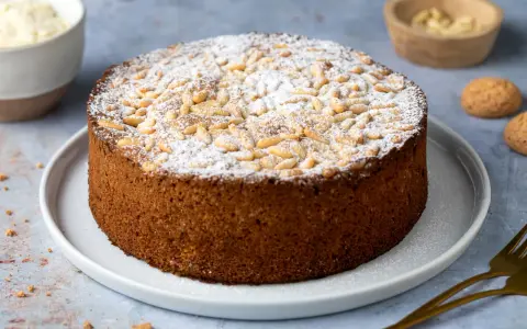 Torta soffice con farina di mandorle, ricoperta di pinoli e zucchero a velo. Perfetta per una pausa golosa.