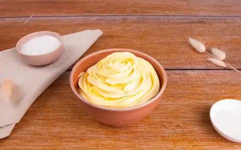 Una ciotola piena di soffice crema al burro, pronta per decorare torte. Accanto, ciotoline con zucchero e decorazioni naturali.